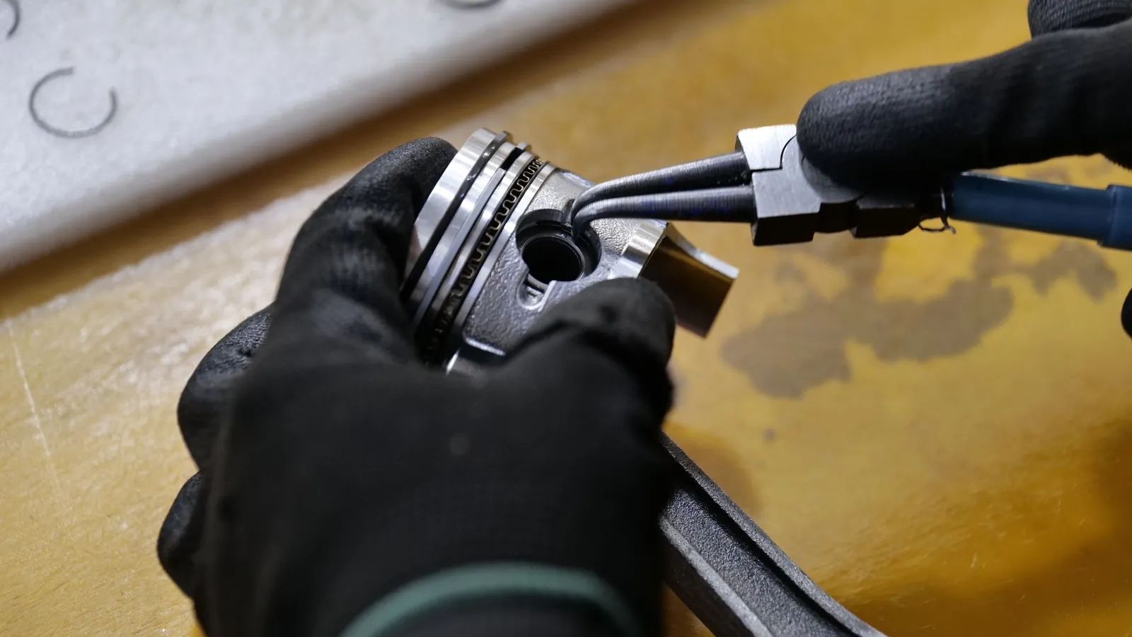 Mains gantées montant un segment sur un piston à l'aide d'une pince
