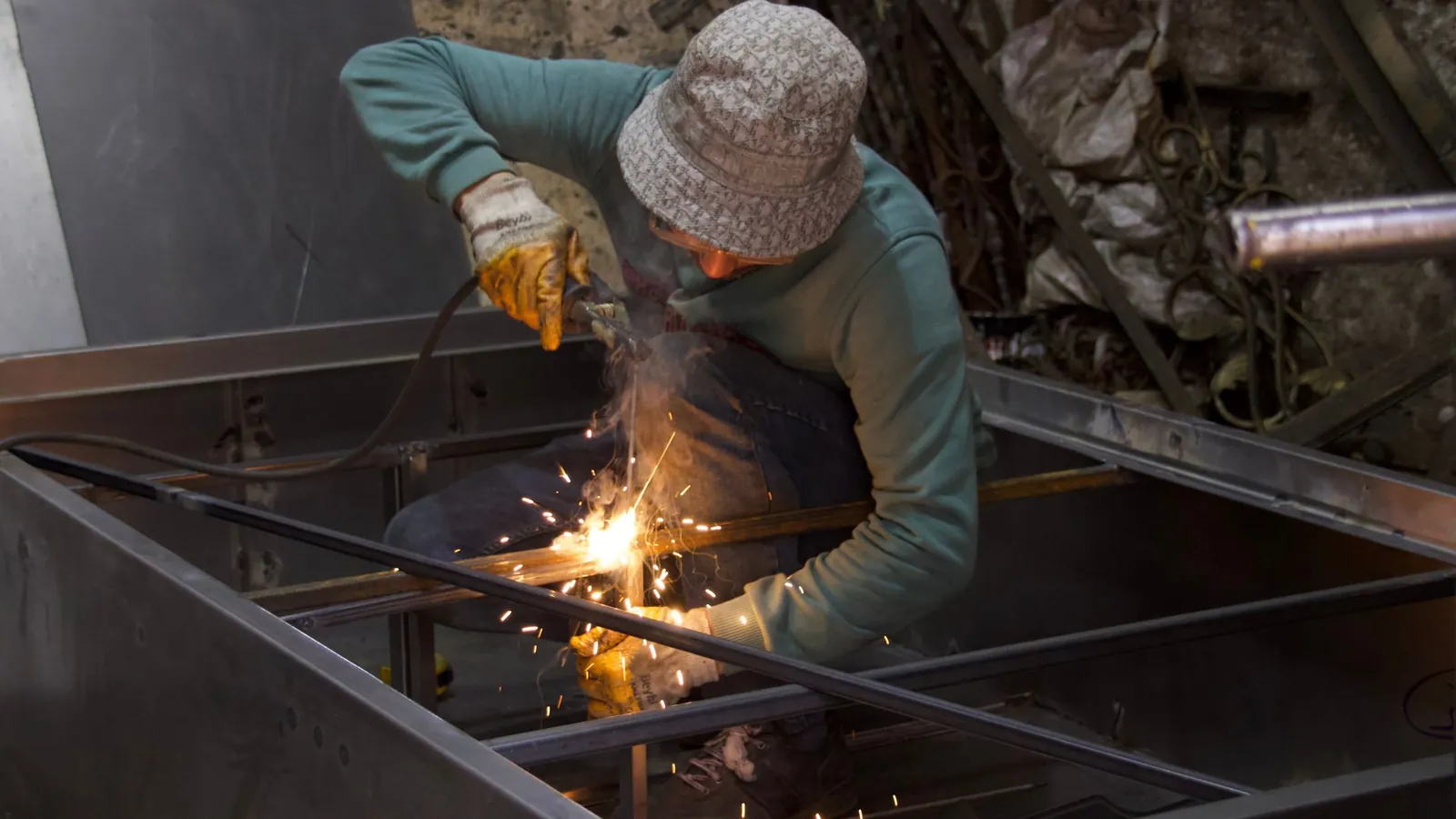 Métallier soudant un cadre en tubes d'acier dans un atelier, étincelles au point de soudure