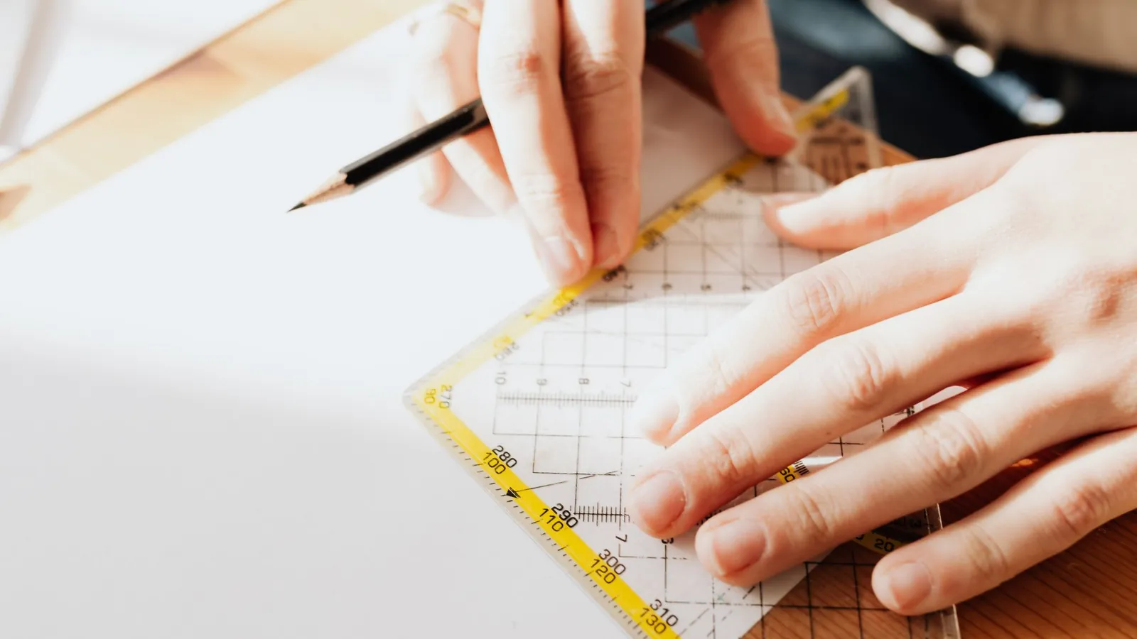 Mains traçant au crayon le long d'une règle graduée sur une feuille