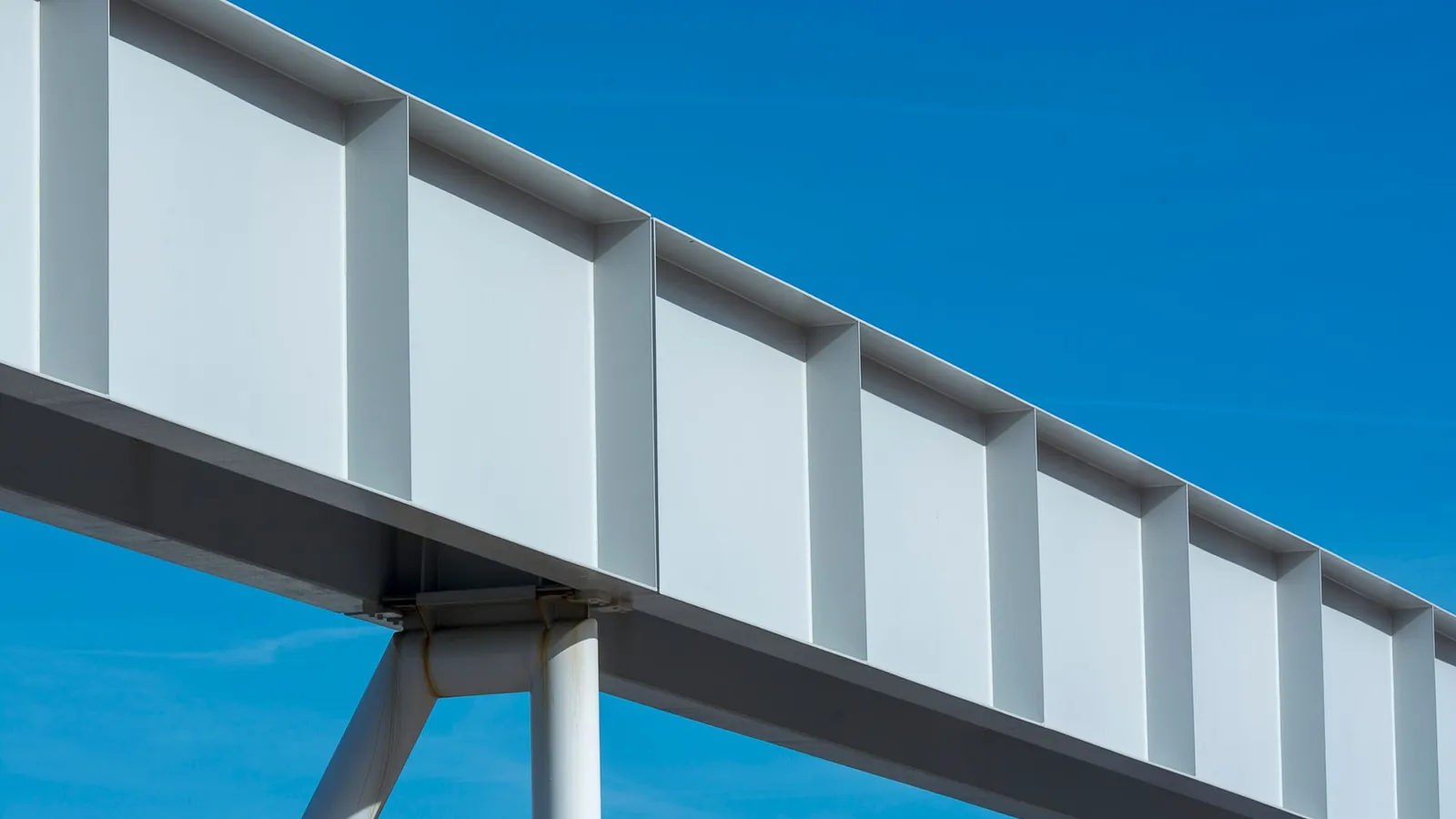 Poutre métallique à âme raidie par des nervures verticales, vue en contre-plongée sur ciel bleu