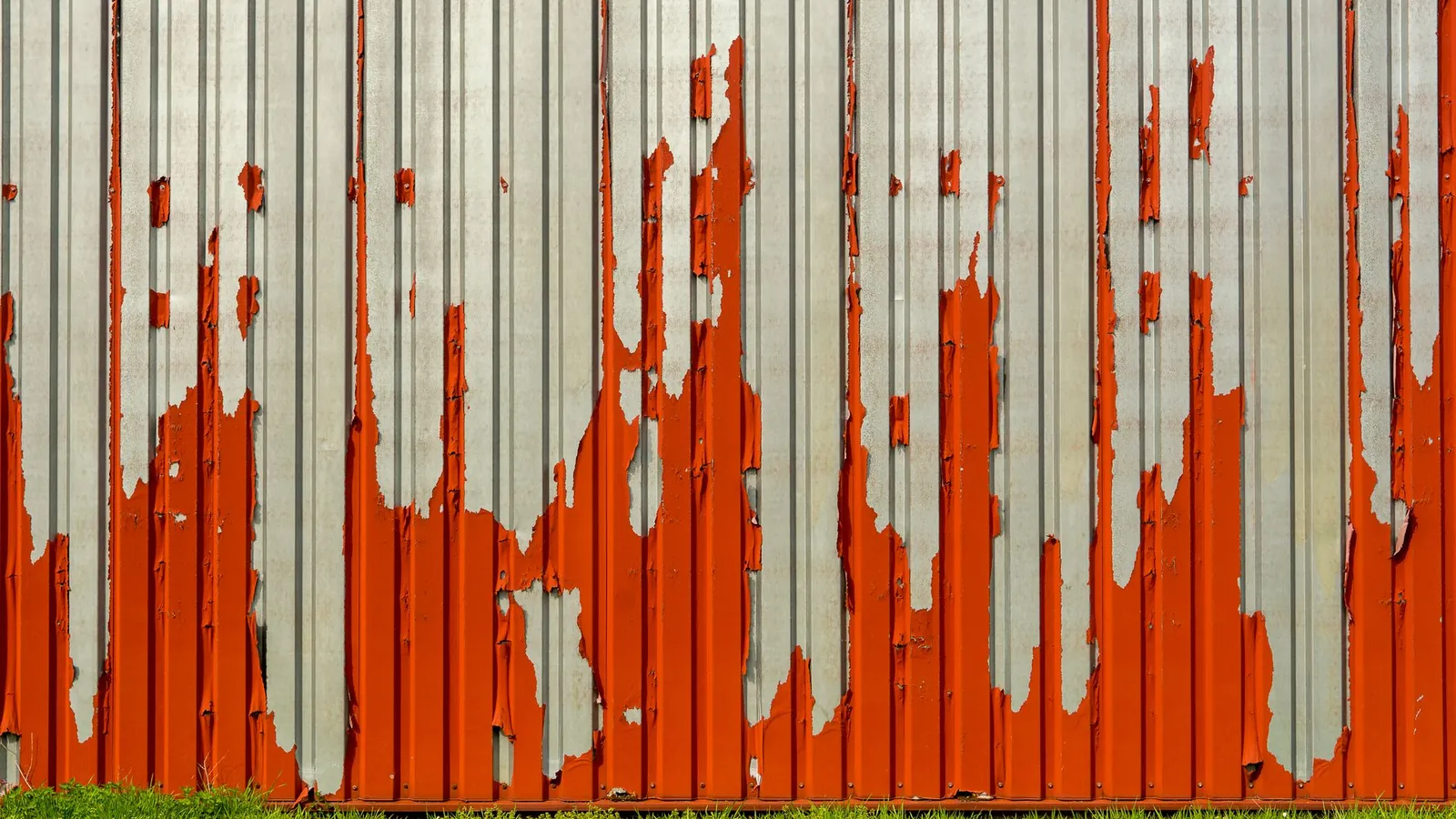 Bardage ondulé en acier galvanisé dont la peinture rouge s'écaille en larges plaques