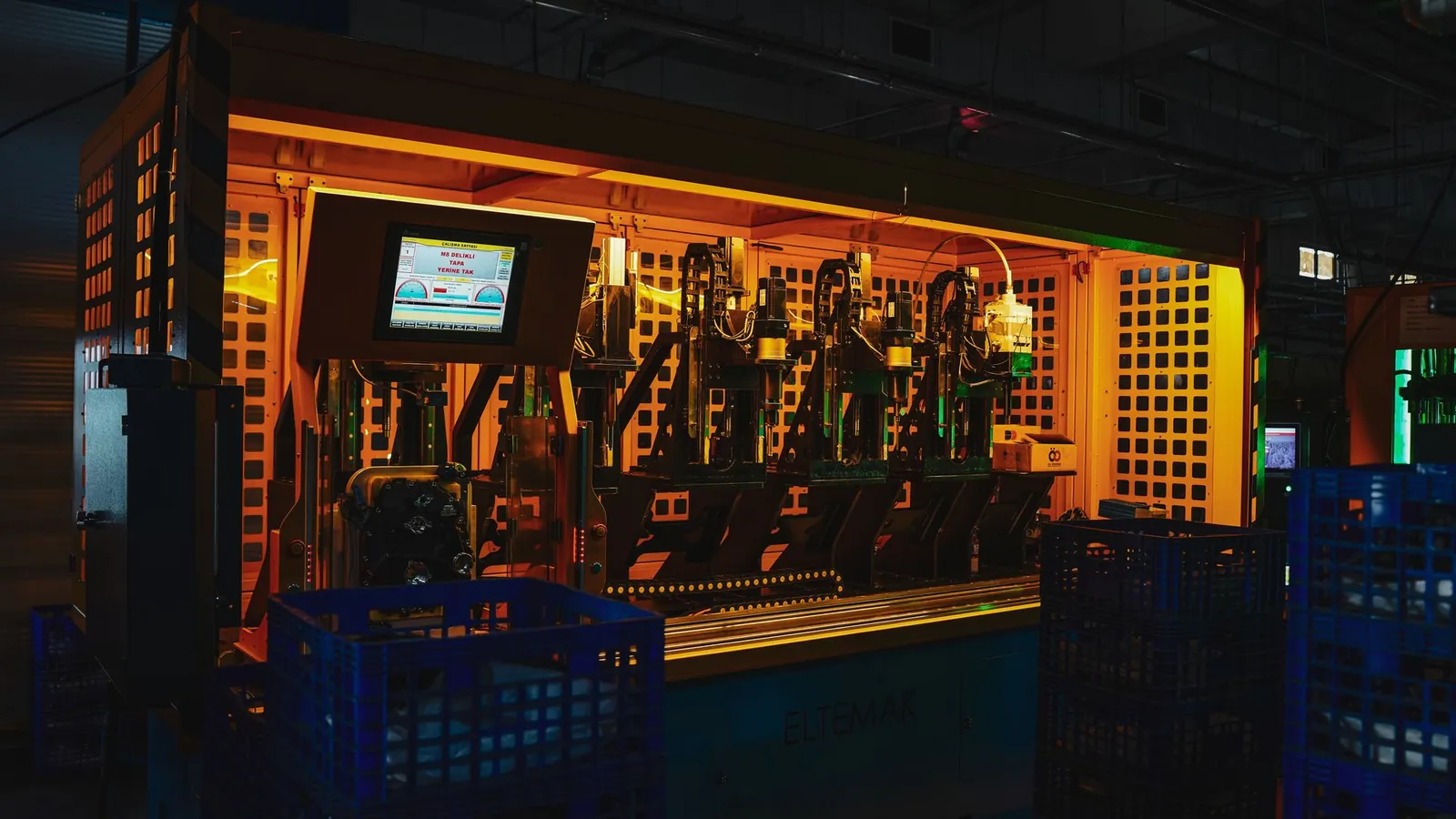 Cellule de production automatisée sous carter grillagé, éclairée en orange, avec son écran de pilotage