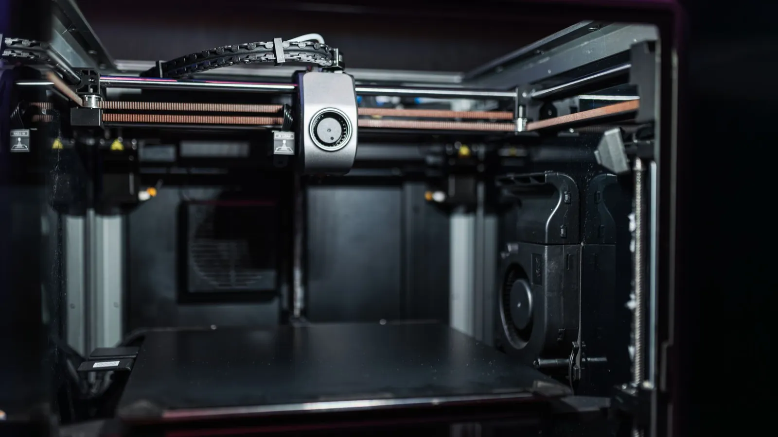Intérieur d'une imprimante 3D à caisson fermé : portique, tête d'impression et plateau noir
