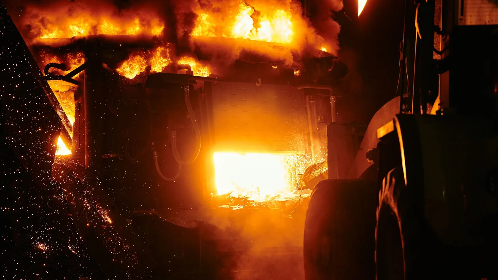 Four industriel ouvert sur une charge incandescente, flammes et étincelles autour du manipulateur