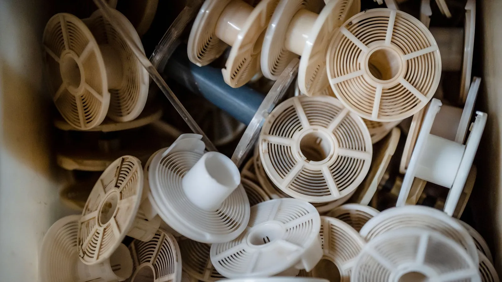 Bobines en plastique blanc injecté, à ajours et rayons moulés, rassemblées en vrac