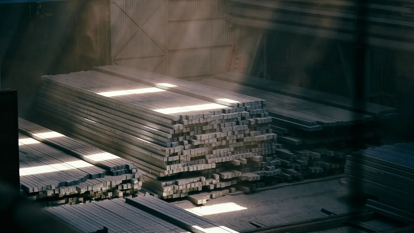 Piles de barres et de profilés en acier stockées dans un entrepôt traversé par la lumière