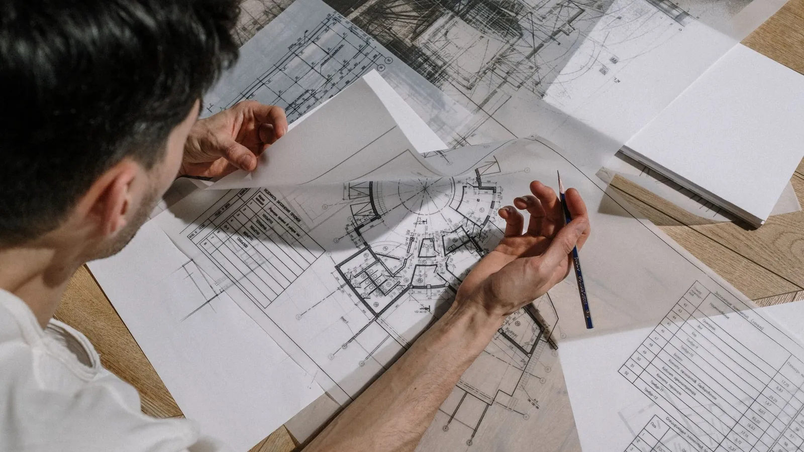 Dessinateur annotant au crayon des plans techniques étalés sur sa table de travail