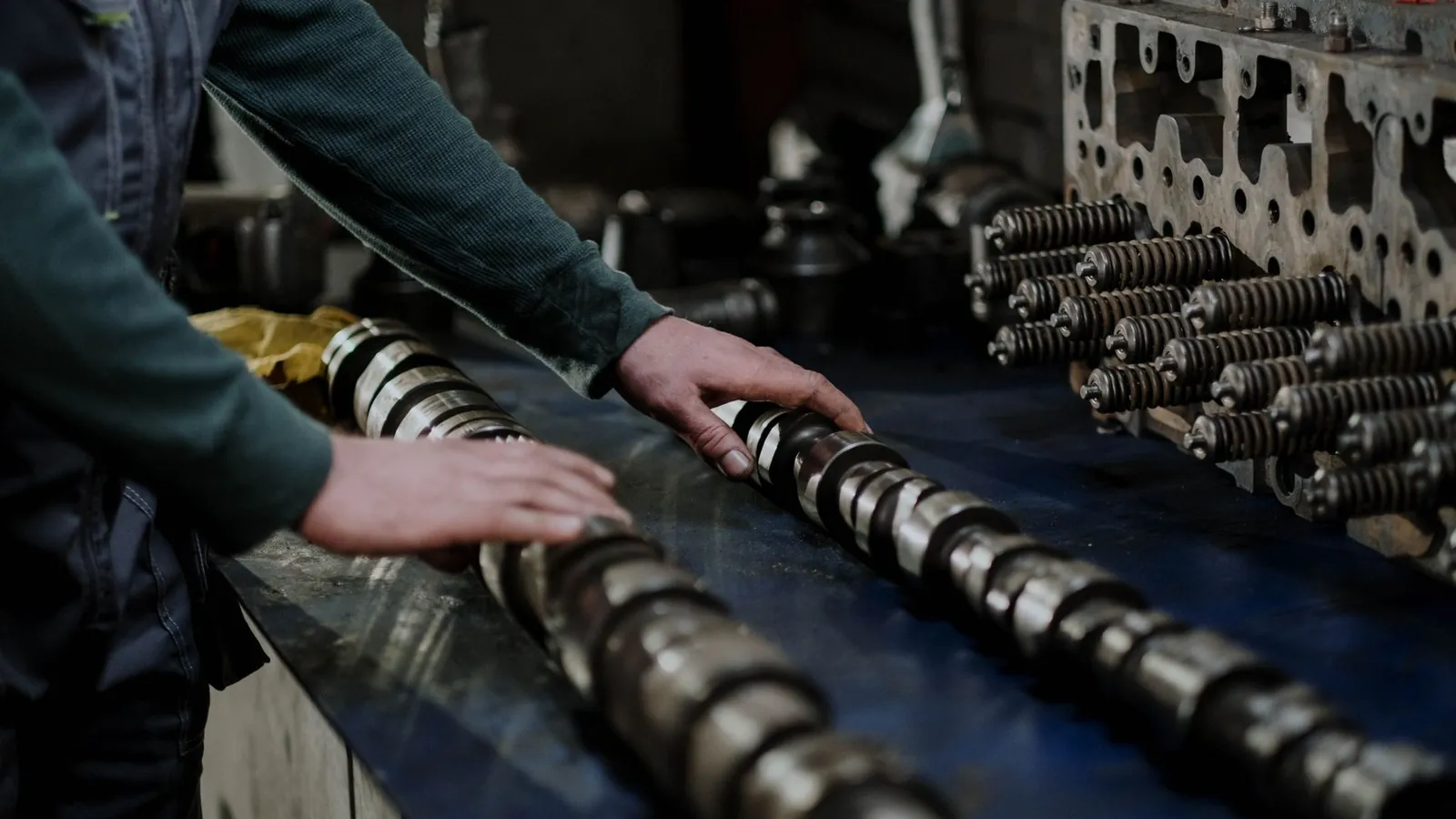 Arbres à cames et pièces de moteur alignés sur un établi, manipulés par un opérateur