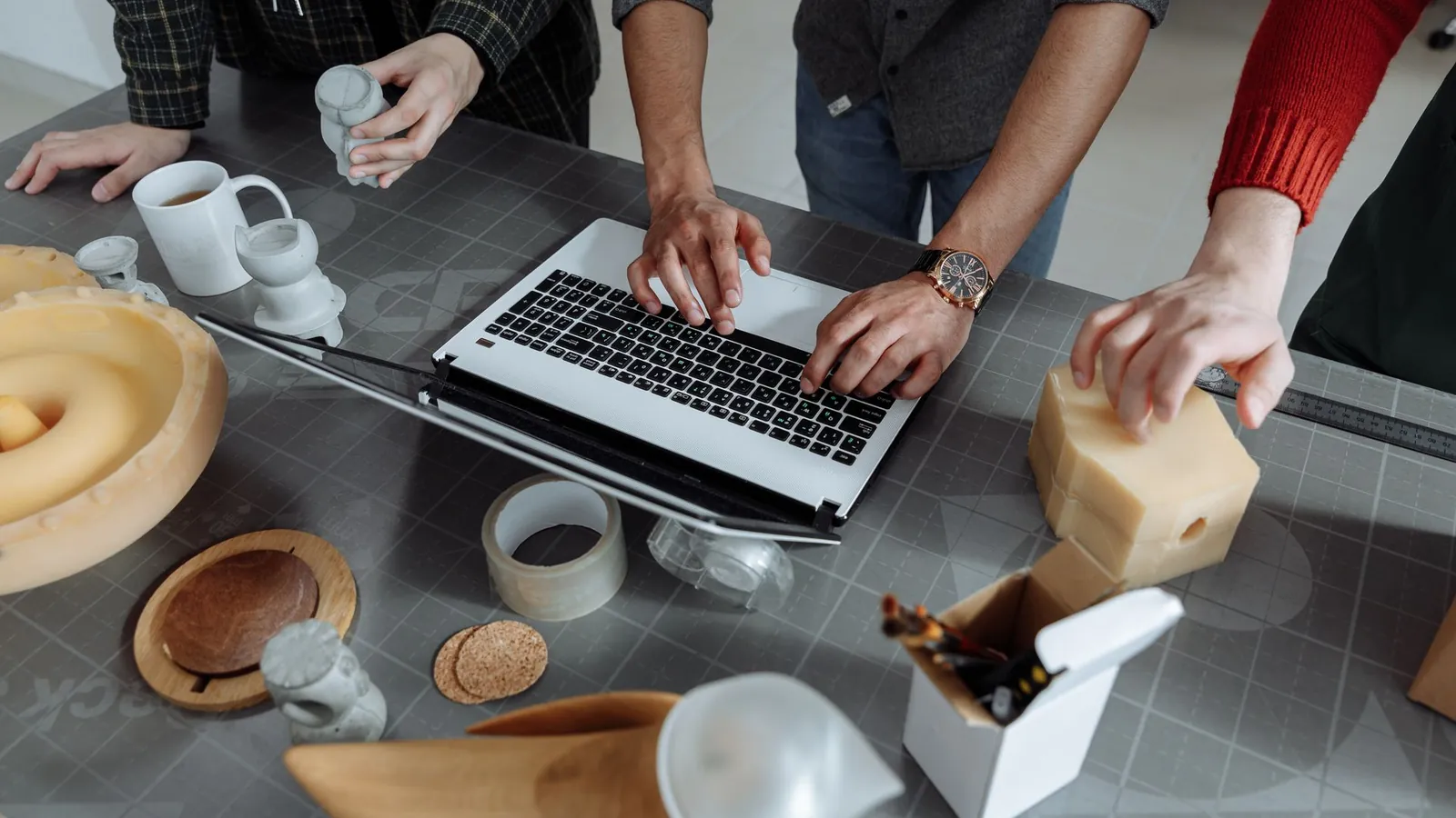 Équipe de conception autour d'une table avec un ordinateur portable, des maquettes imprimées et des modèles en résine