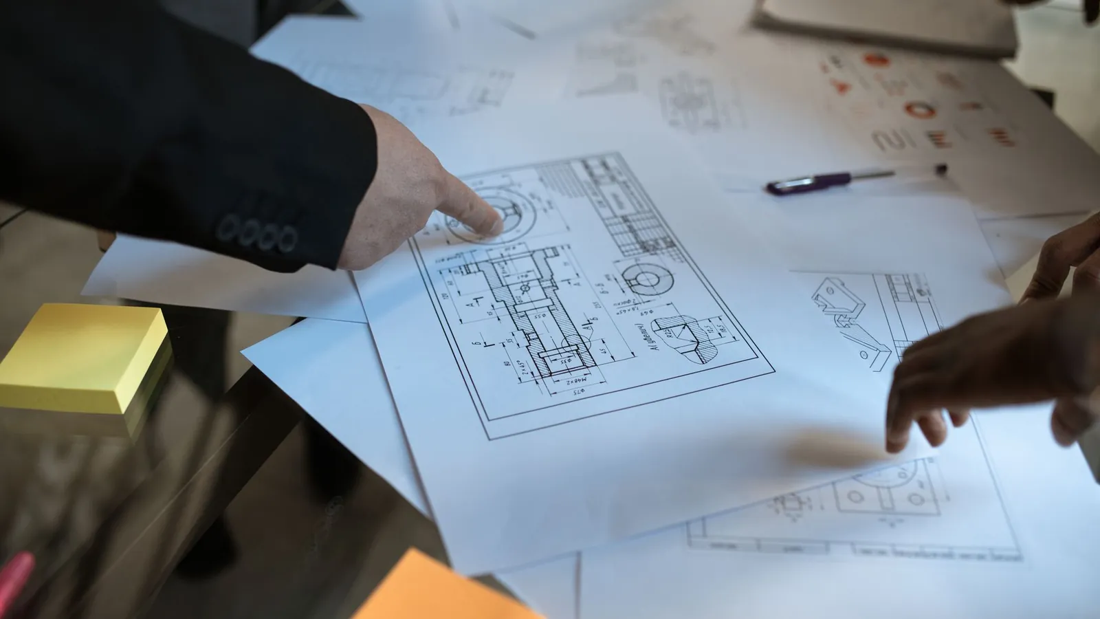 Deux personnes relisant des plans techniques étalés sur une table, l'une pointant un détail du dessin