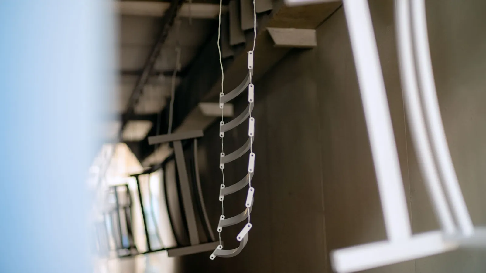 Petites pièces métalliques cintrées enfilées sur un fil d'accrochage, sous le convoyeur d'un atelier de laquage