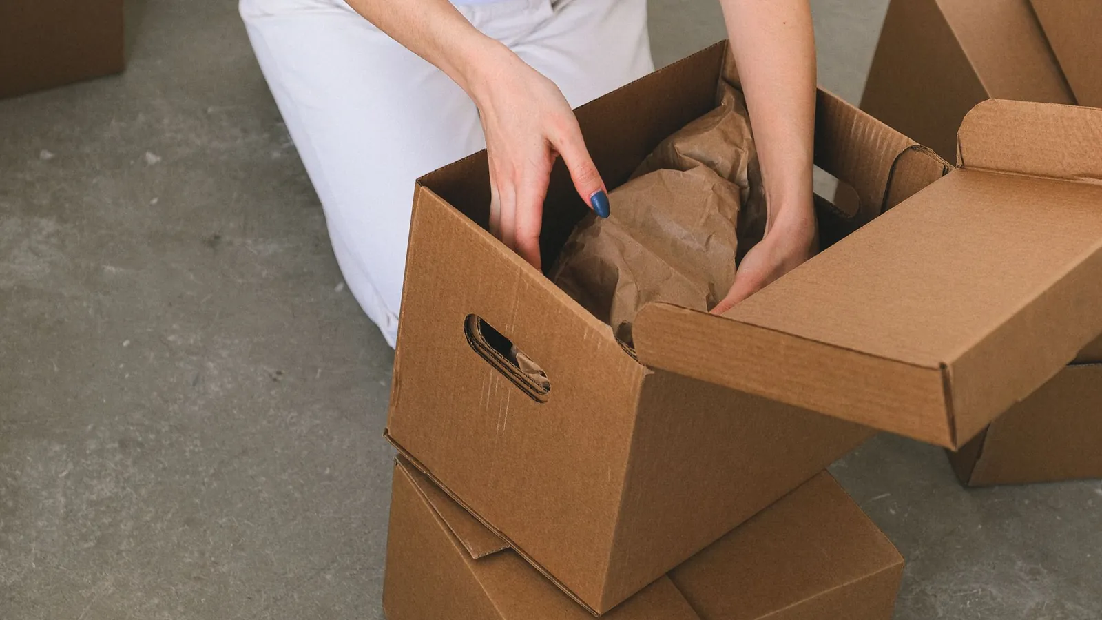 Calage au papier kraft glissé dans un carton ondulé à poignées, posé sur d'autres cartons