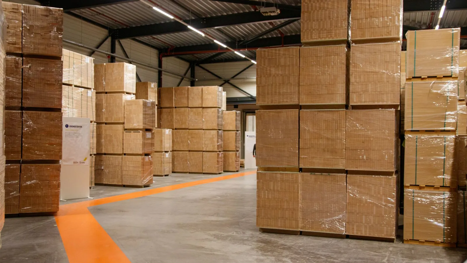 Palettes de cartons filmés stockées dans un entrepôt, allée balisée par un marquage orange au sol