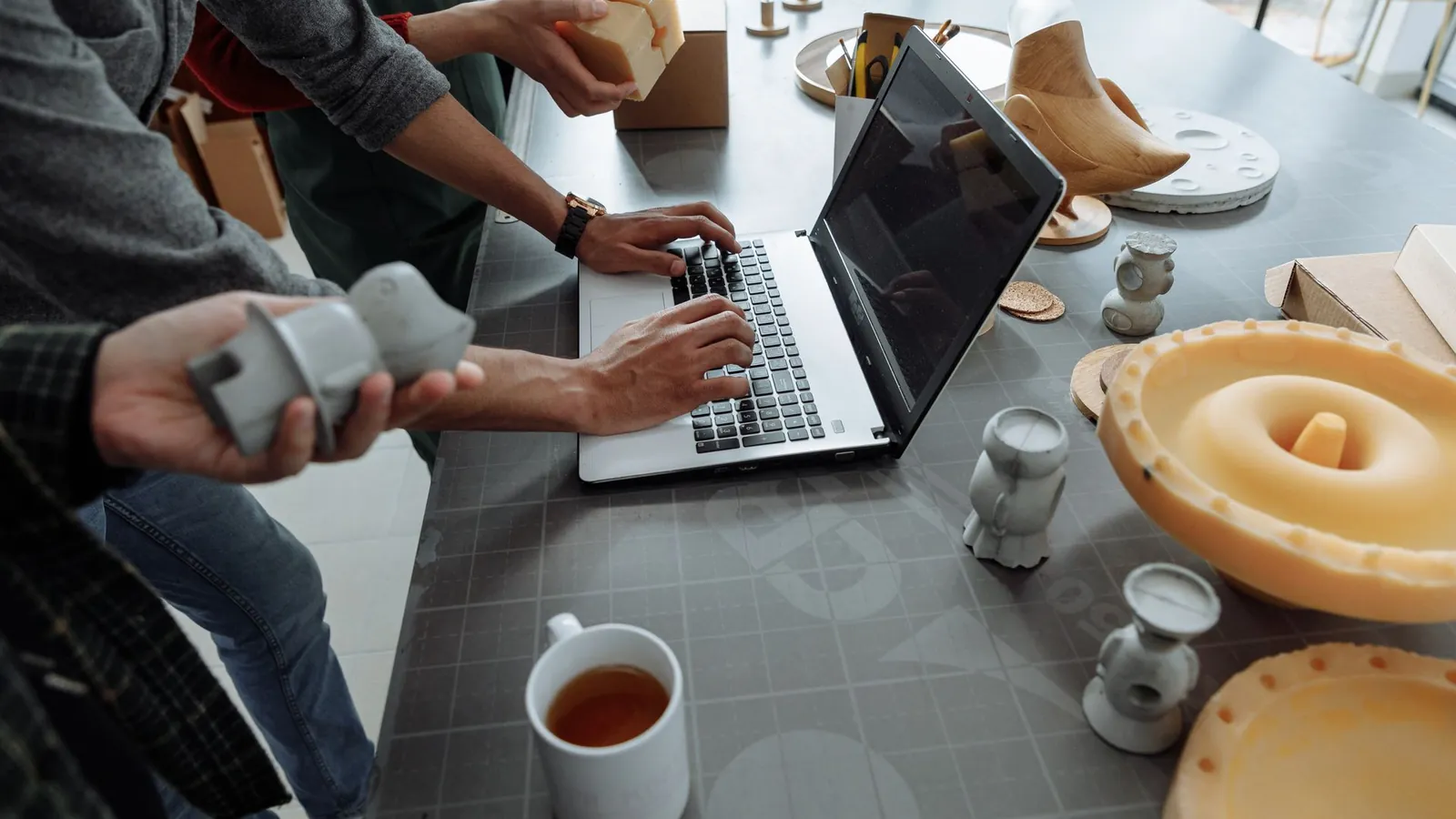 Prototypes imprimés en 3D et maquettes en résine examinés autour d'un ordinateur portable sur une table d'atelier