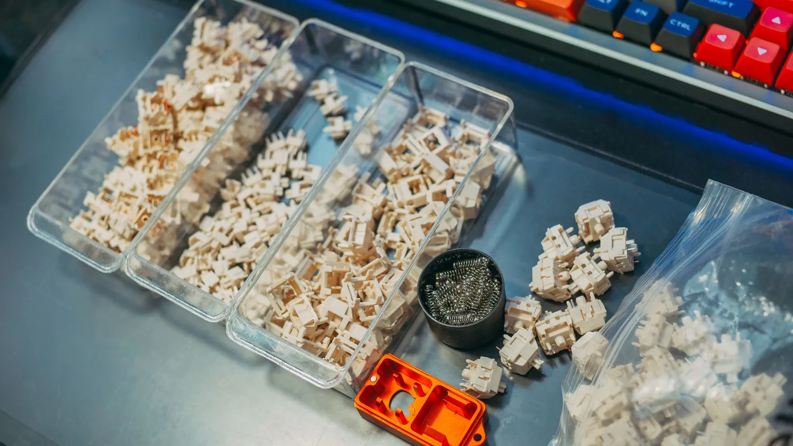 Petites pièces en plastique injecté triées dans des bacs transparents, à côté d'un boîtier usiné orange