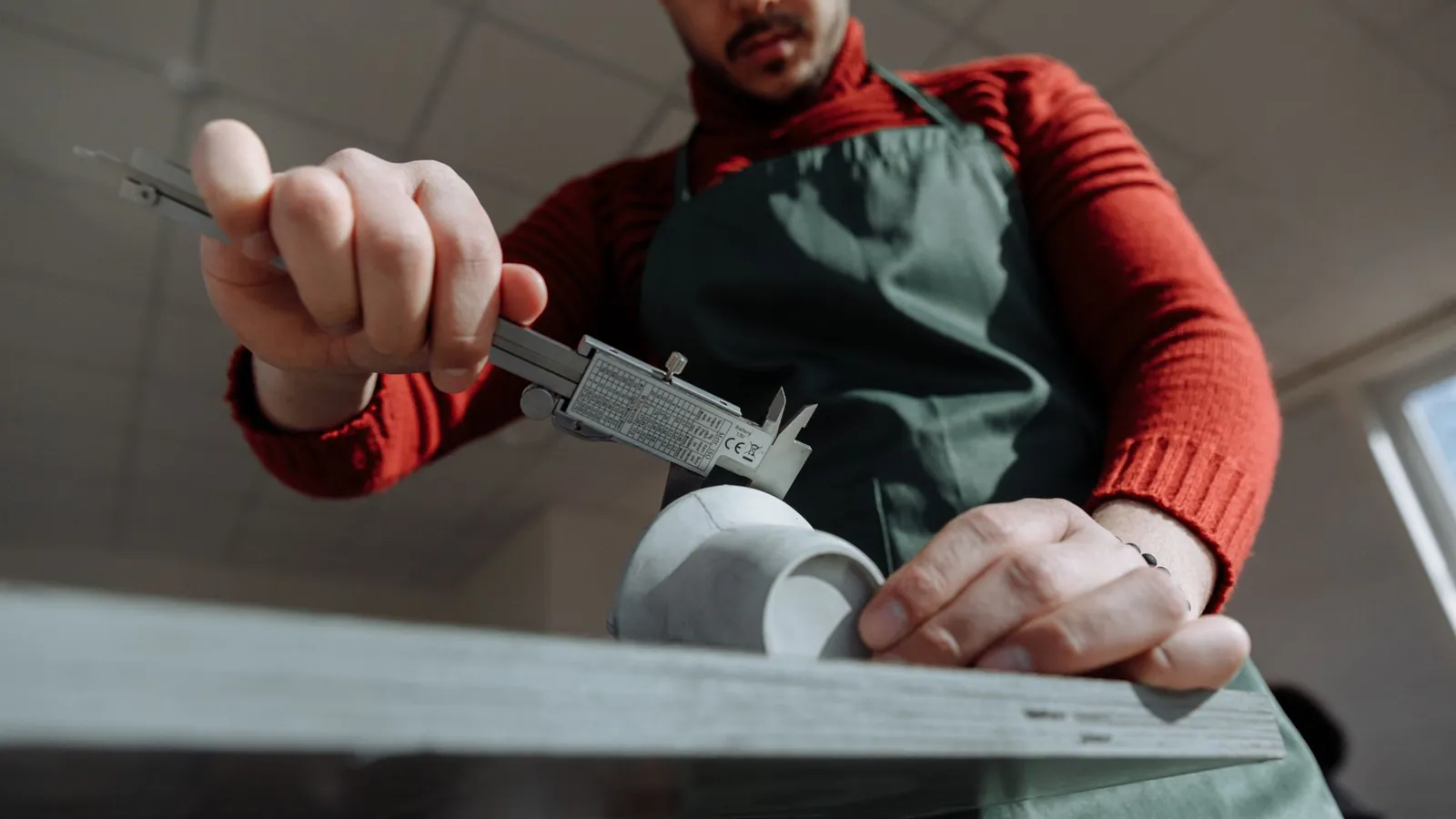 Contrôle au pied à coulisse d'une pièce blanche maintenue sur une planche, gros plan sur les mains