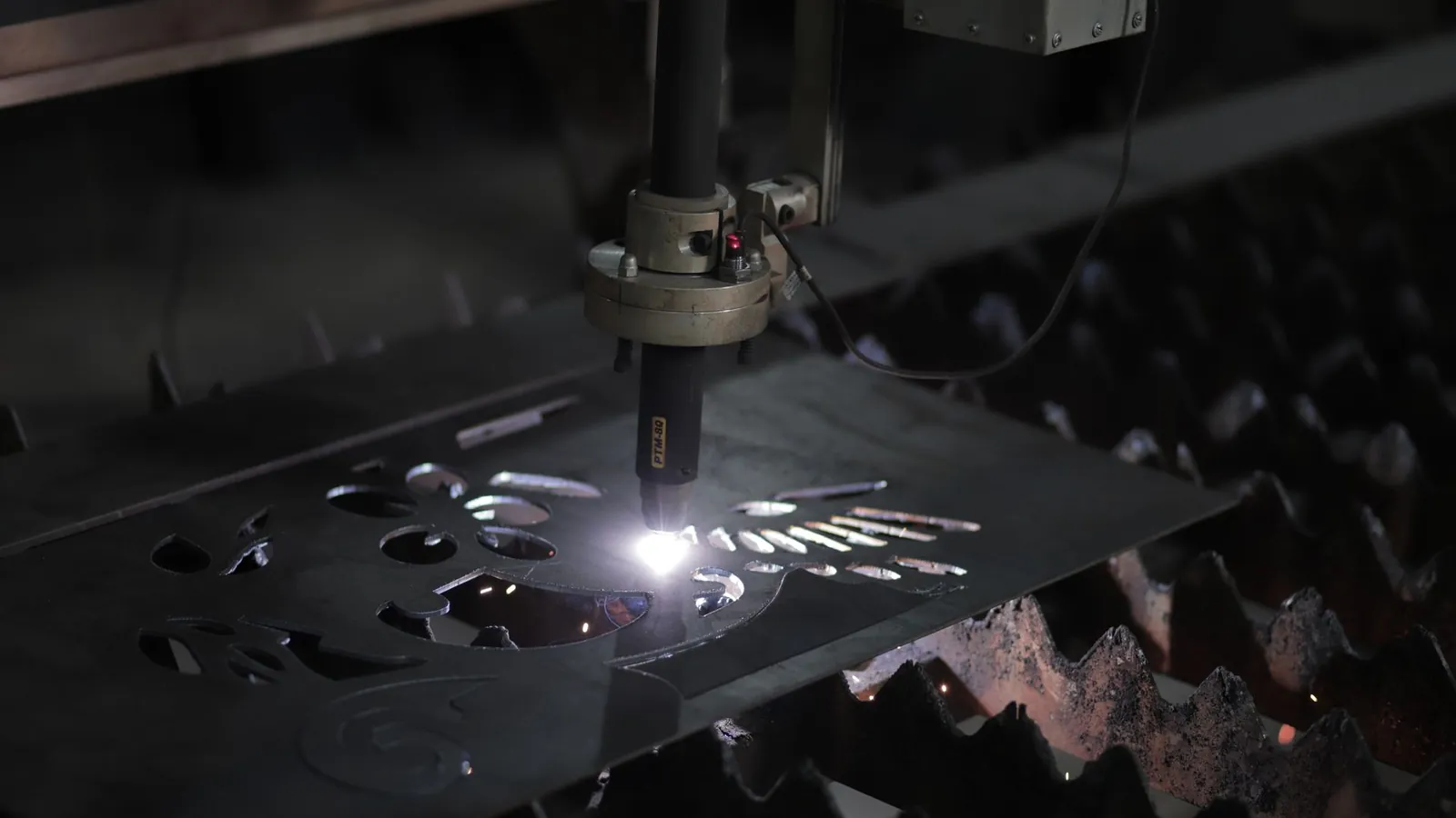 Torche de découpe plasma traversant une tôle d'acier sur une table à grille, formes déjà évidées