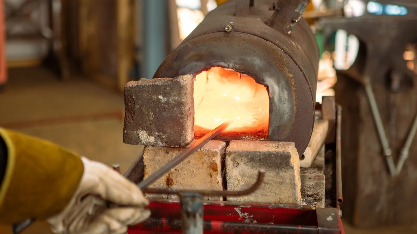 Barre d'acier chauffée dans un four à gaz garni de briques réfractaires, tenue à la pince par une main gantée