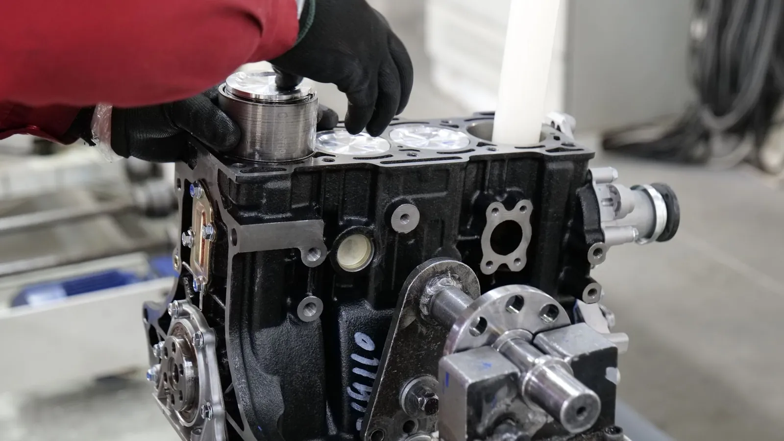 Opérateur aux gants noirs engageant un piston dans un bloc moteur noir sur un poste de montage d'usine