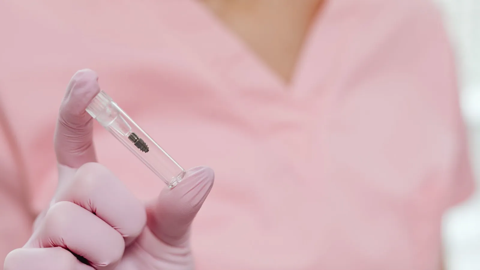 Main gantée de rose tenant un implant dentaire en titane, conditionné dans son tube stérile
