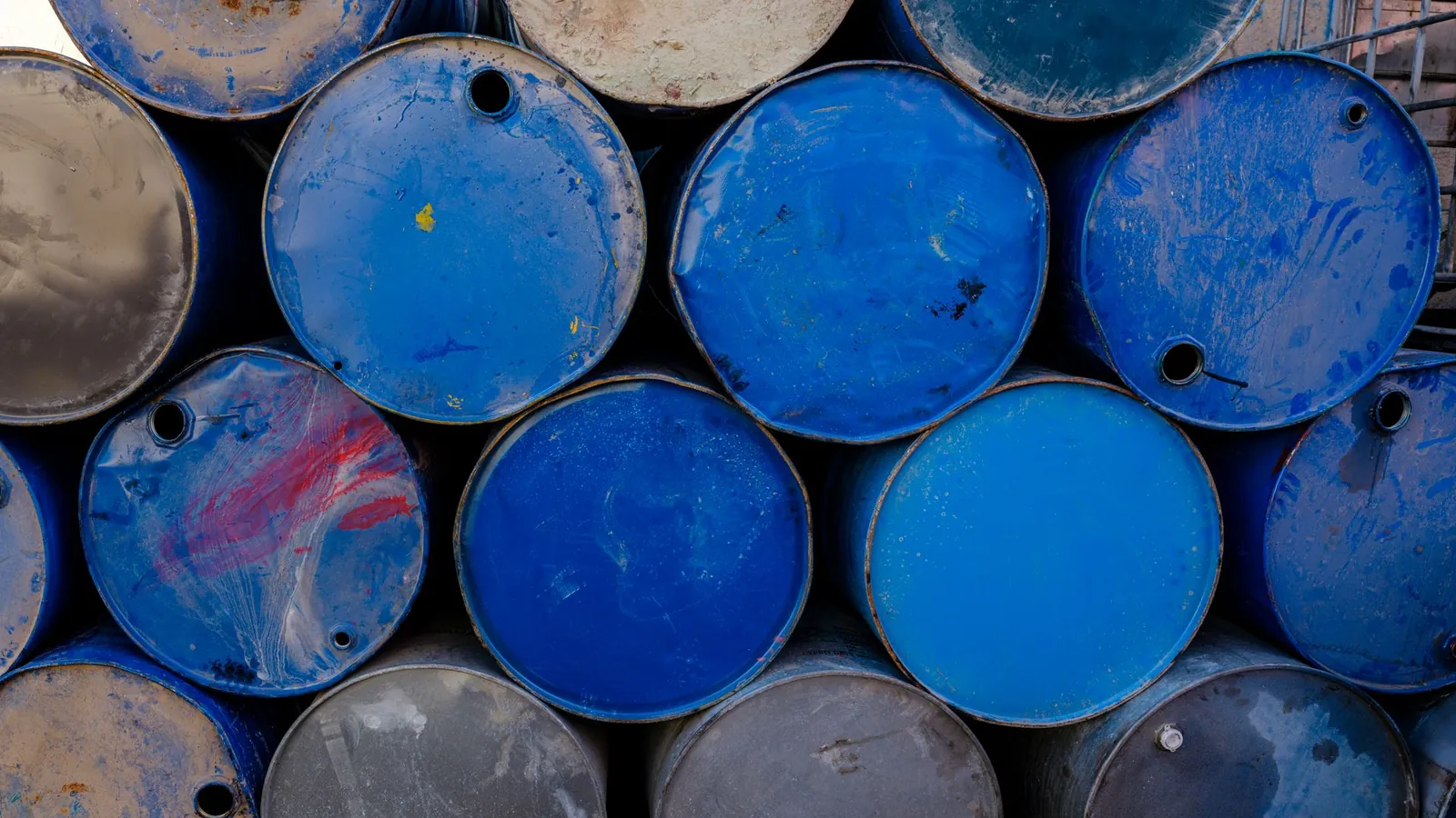 Pile de fûts métalliques bleus à la peinture écaillée, stockés en plein air