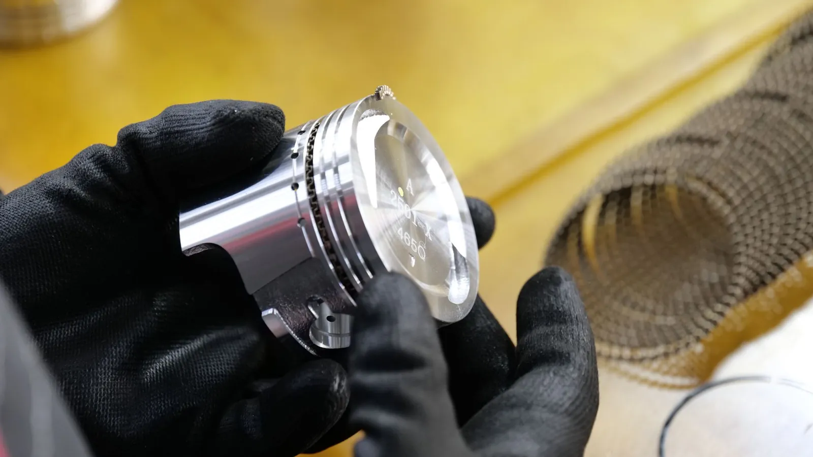 Mains gantées de noir tenant un piston en aluminium usiné pour l'examiner avant montage