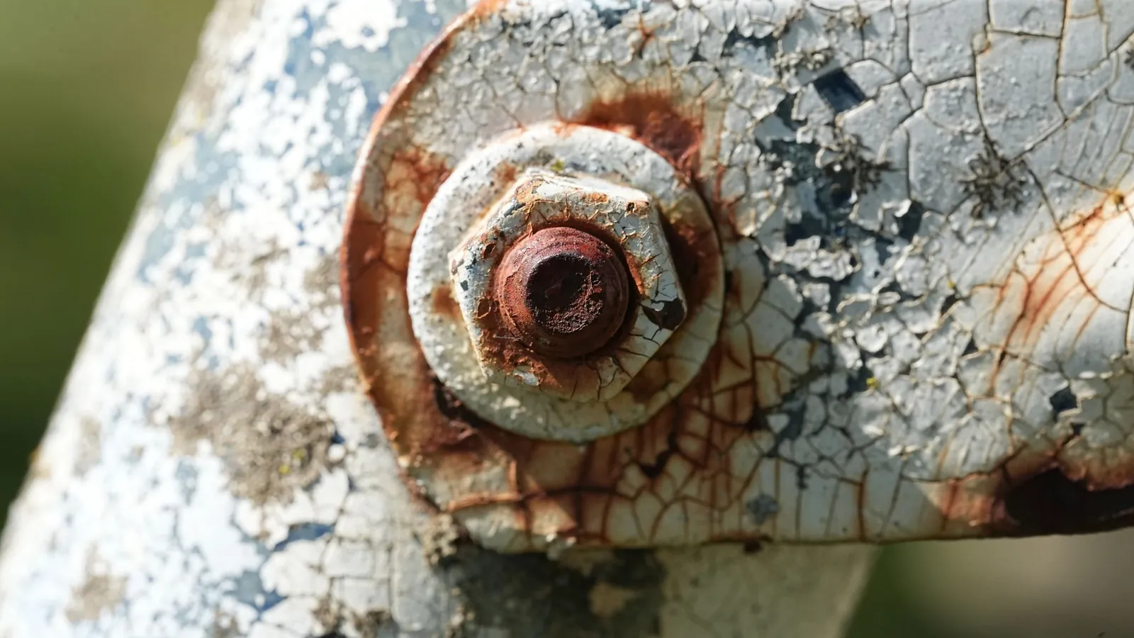 Écrou et rondelle rouillés sur une pièce d'acier dont la peinture blanche s'écaille autour de la fixation