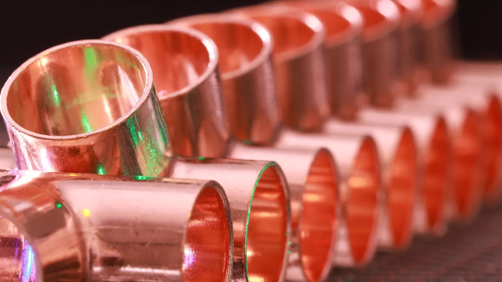Rangée de manchons en cuivre brillant posés sur une grille, reflets verts sur le métal