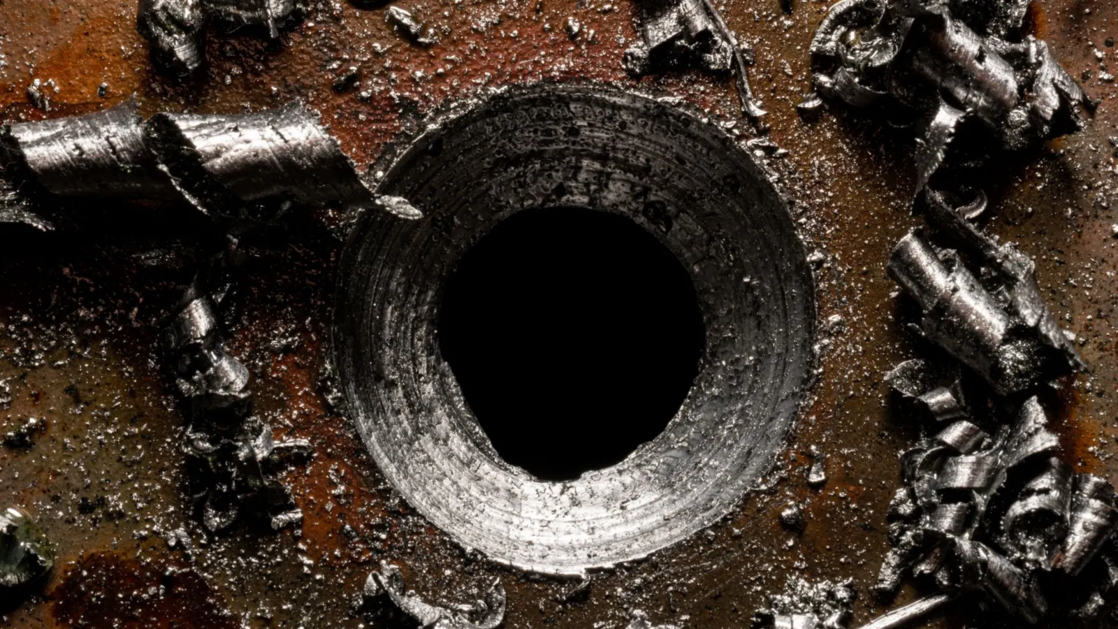 Trou percé et chanfreiné dans une plaque d'acier, entouré de copeaux métalliques en spirale