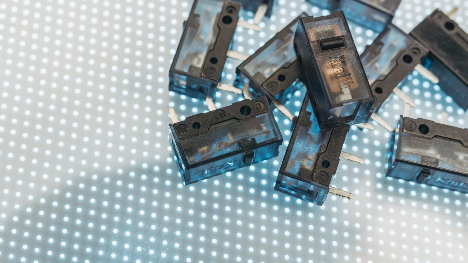 Petits boîtiers électriques en plastique translucide bleuté éparpillés sur une surface lumineuse à points blancs