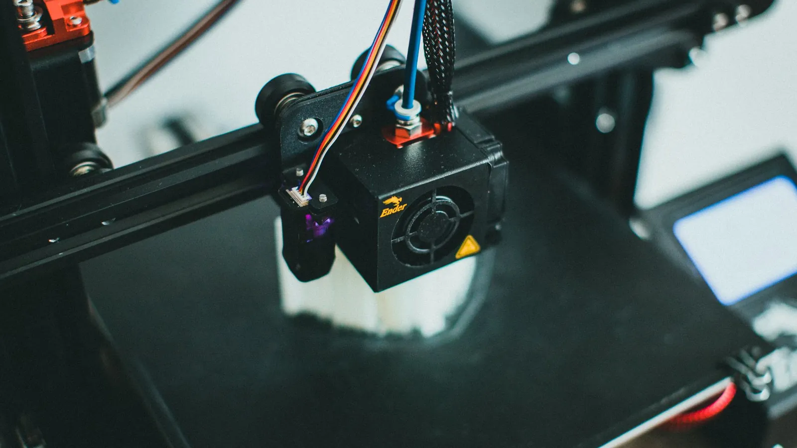 Tête d'impression d'une imprimante 3D à dépôt de fil, ventilateur et câbles colorés, au-dessus d'une pièce en cours
