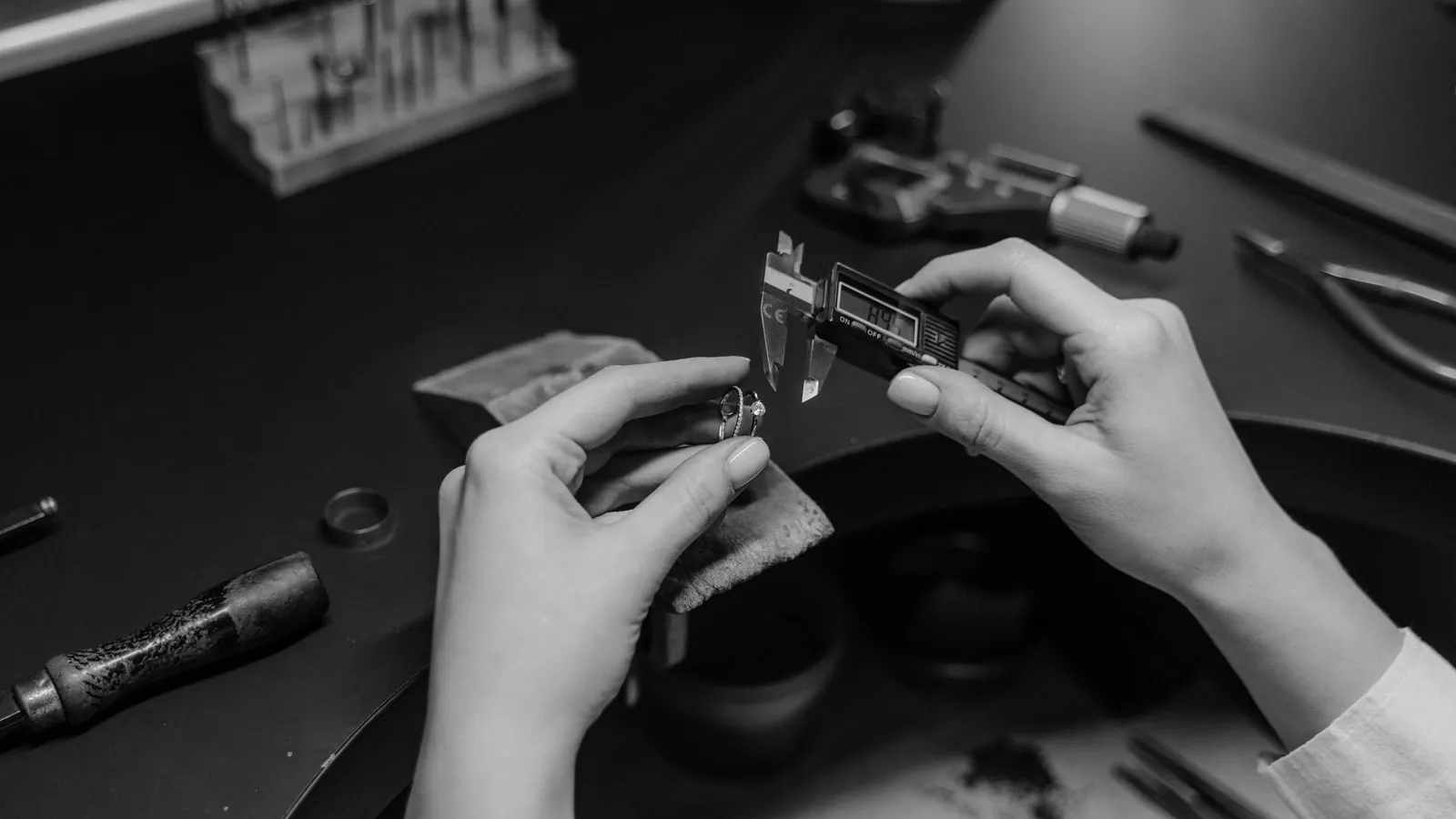 Mains mesurant au pied à coulisse numérique une petite bague métallique, outils de précision sur l'établi, en noir et blanc