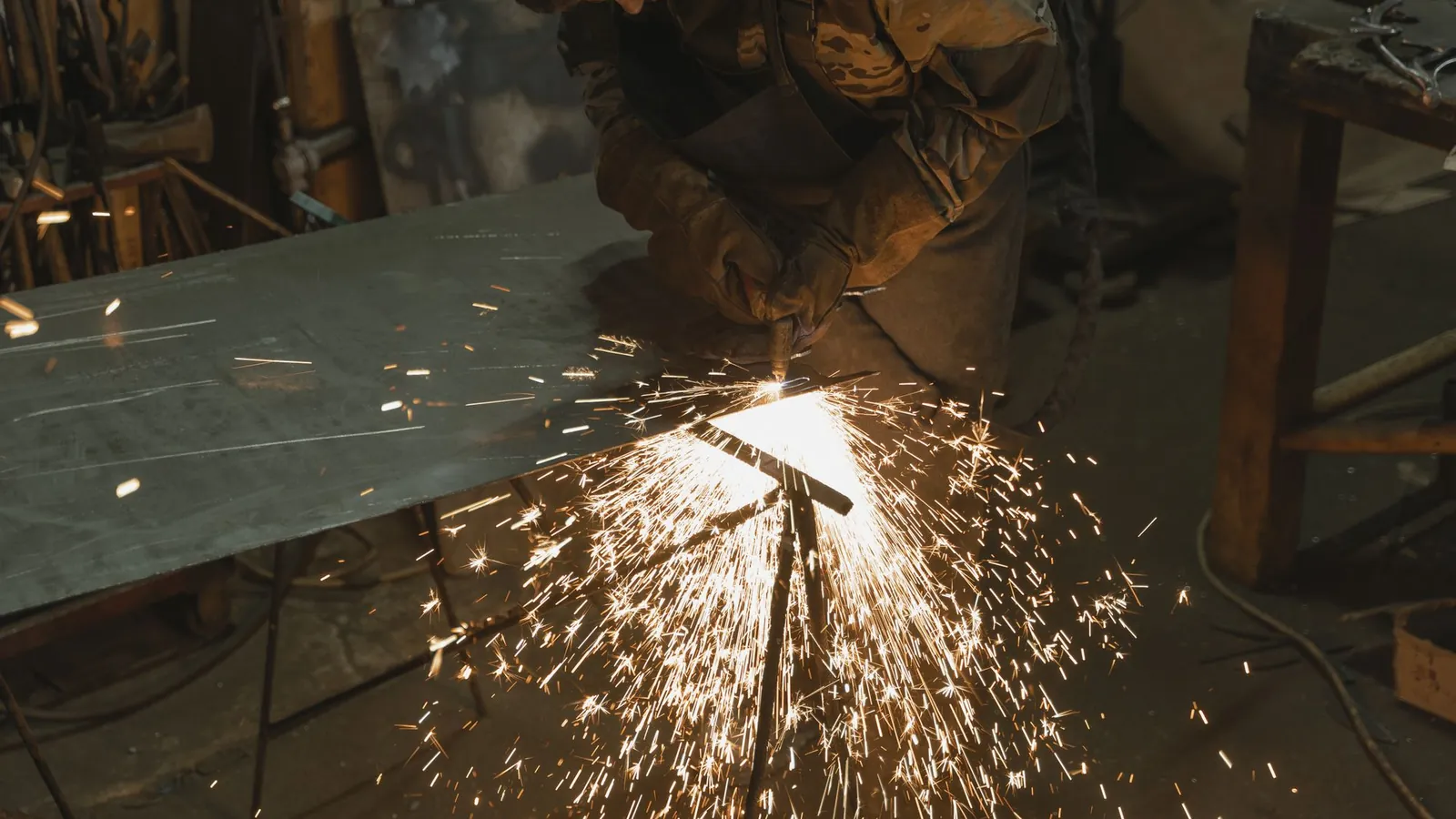 Découpe d'une tôle d'acier posée sur un établi, gerbe d'étincelles sous la torche dans un atelier sombre