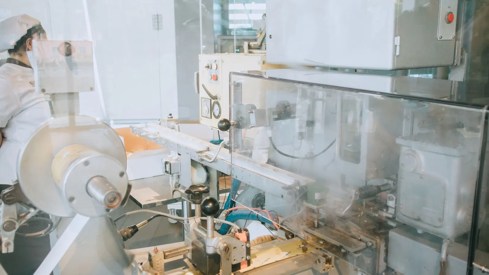 Machine de production automatique protégée par des carters transparents, opératrice en blouse en arrière-plan