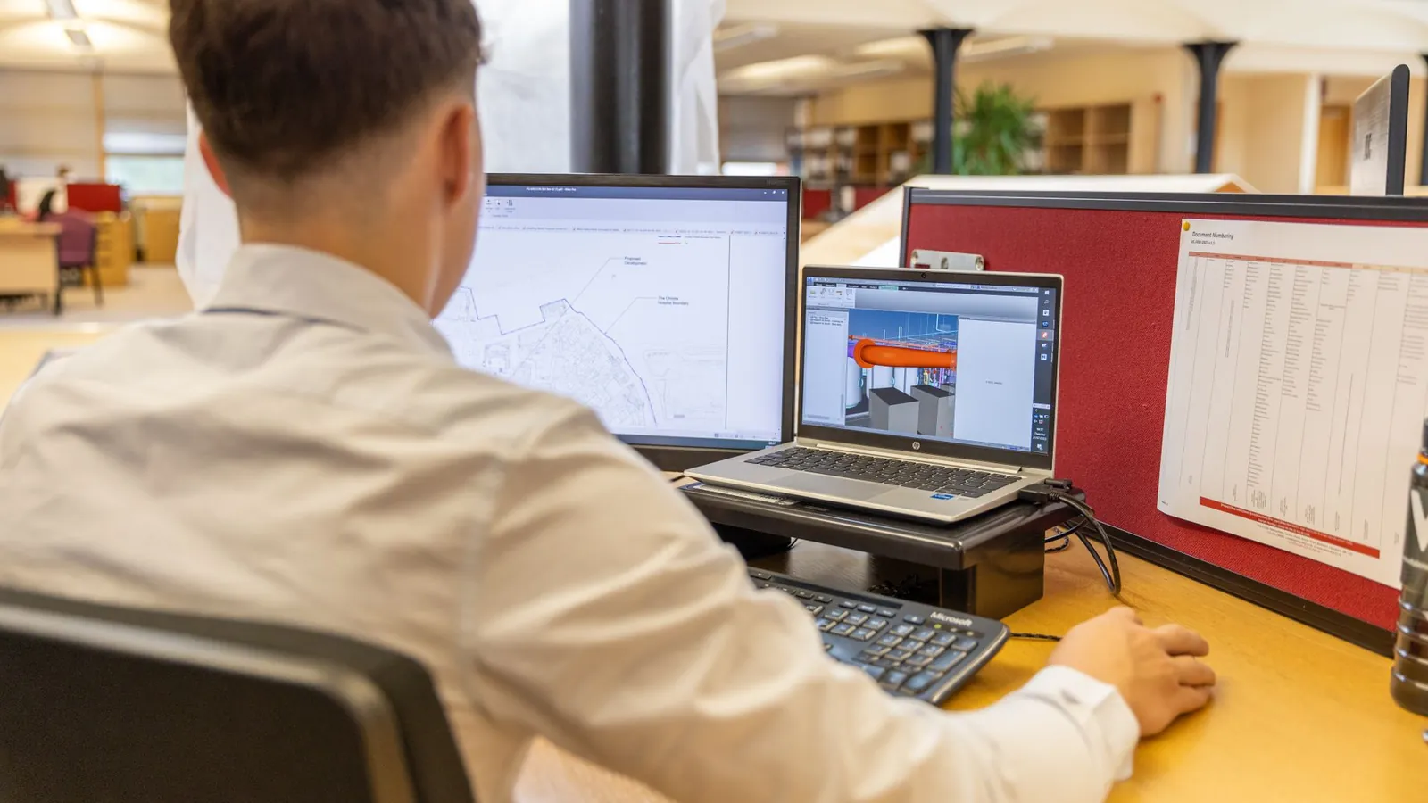 Projeteur de dos travaillant sur un modèle 3D et un plan, devant deux écrans dans un bureau d'études