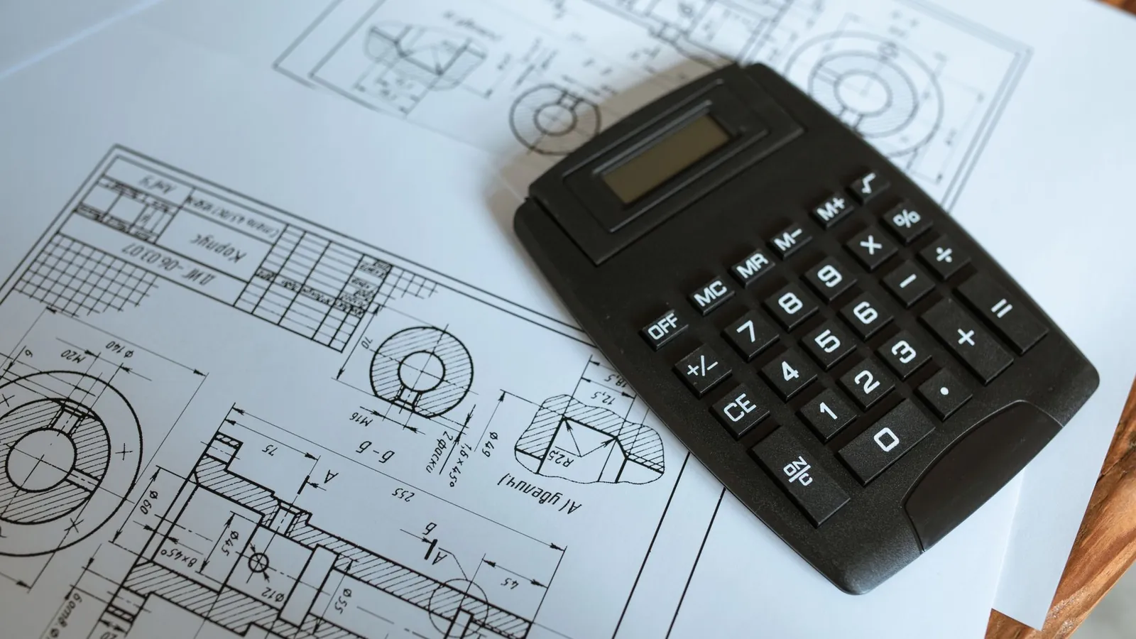 Calculatrice posée sur un plan de définition mécanique avec coupes et cotes