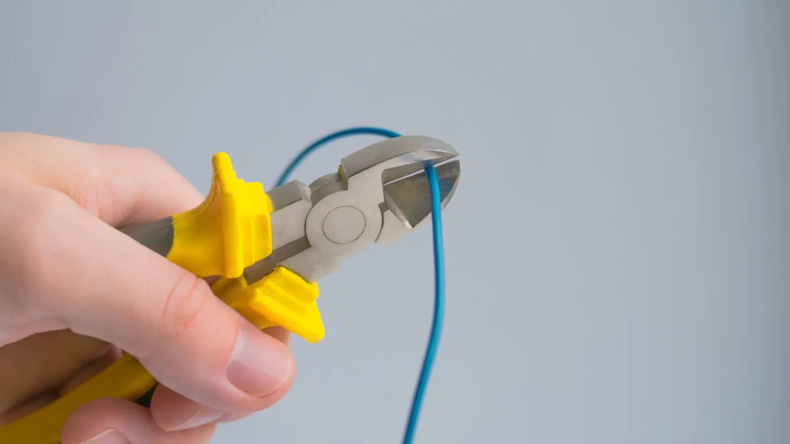 Main tenant une pince coupante à poignées jaunes pour sectionner un fil électrique bleu