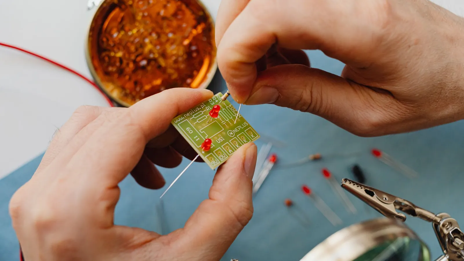 Mains brasant les pattes de diodes traversantes sur une petite carte, boîte de flux en arrière-plan