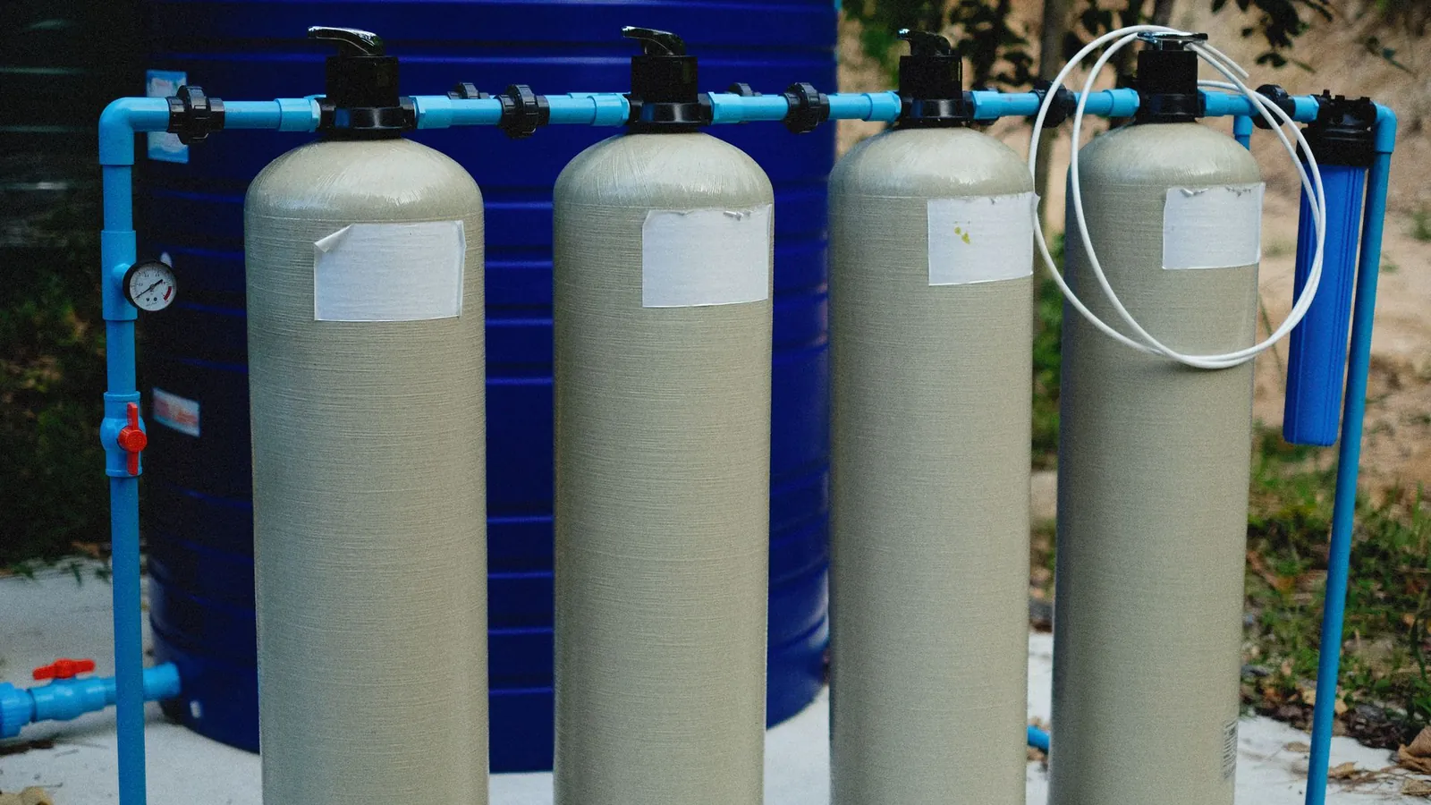 Réservoirs de filtration reliés par des tuyauteries en PVC bleu devant une grande cuve en polyéthylène