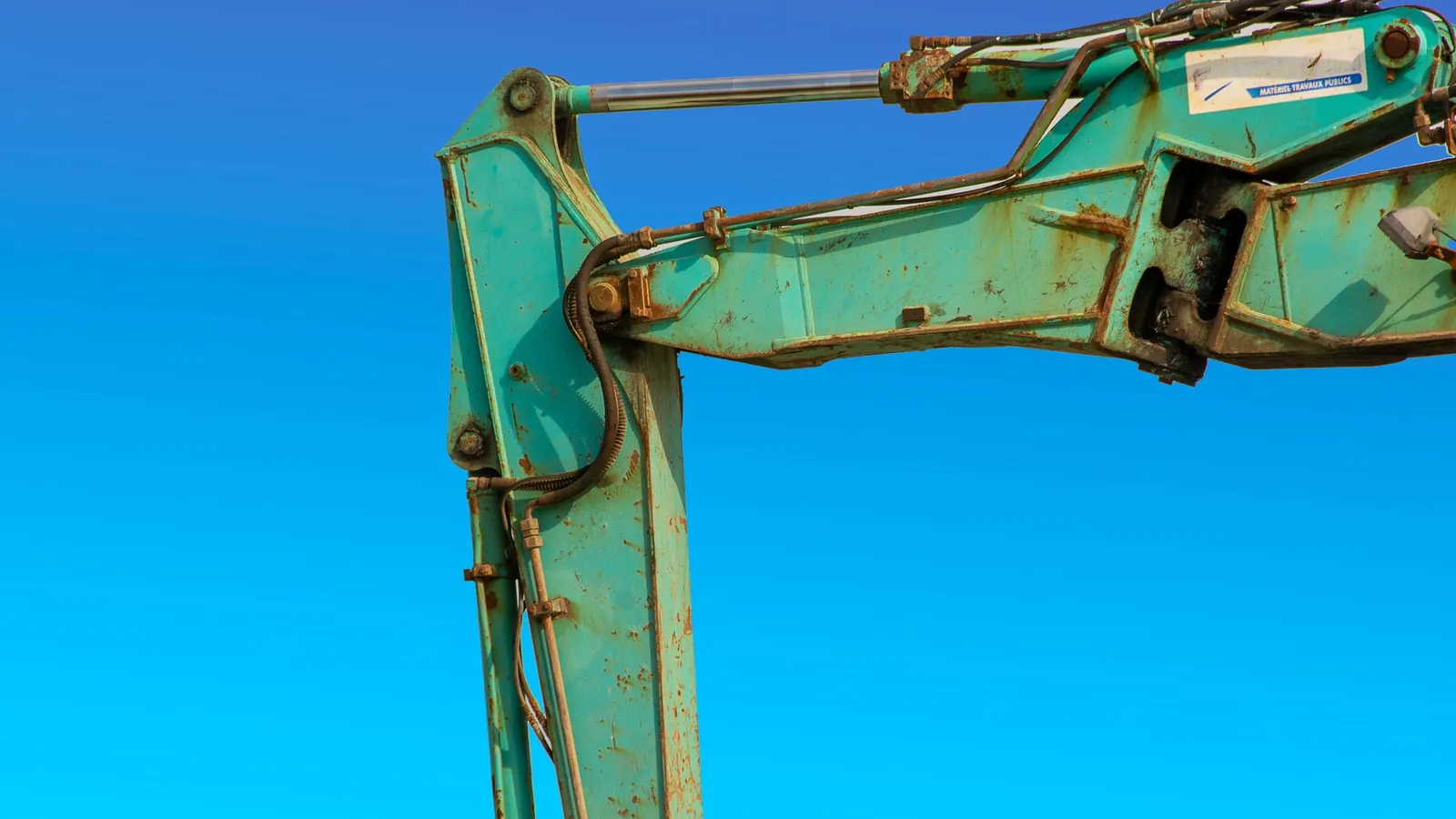 Bras de pelle hydraulique et tiges de vérins chromées se découpant sur un ciel bleu