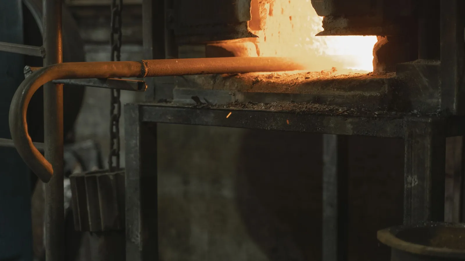 Barre d'acier portée au rouge à la sortie d'un four de forge, dans un atelier sombre