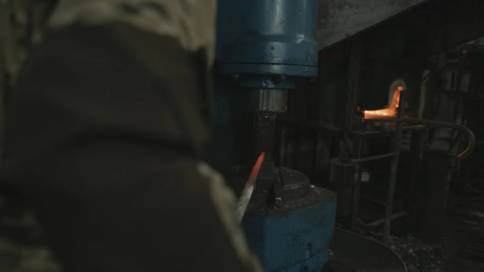 Marteau-pilon bleu d'un atelier de forge, four allumé en arrière-plan