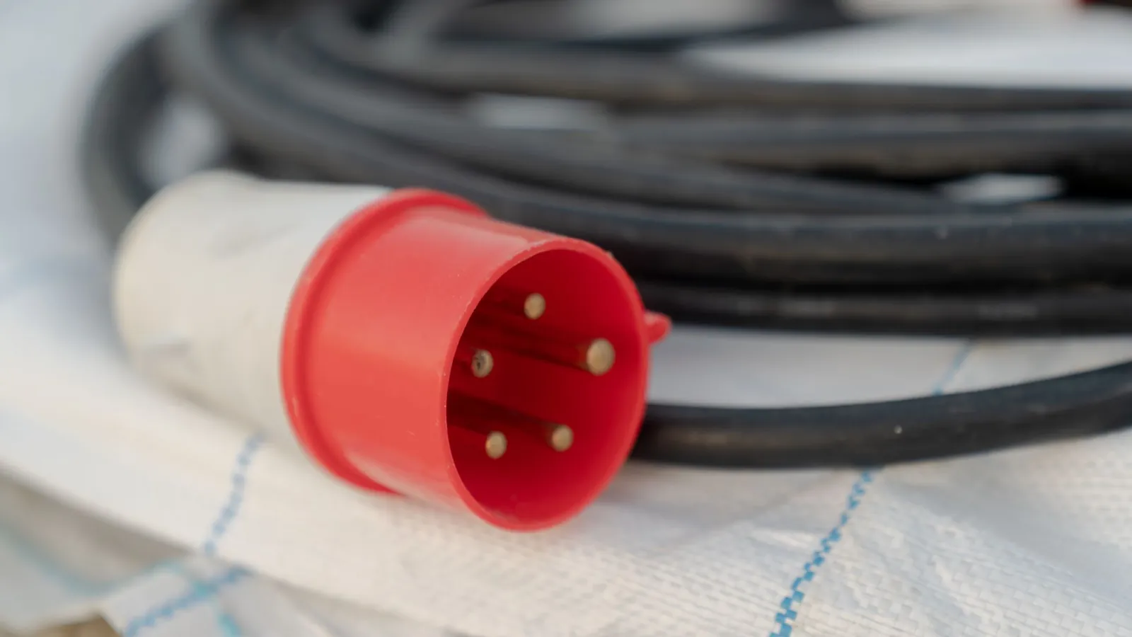 Câble souple noir enroulé terminé par une fiche industrielle rouge à cinq broches