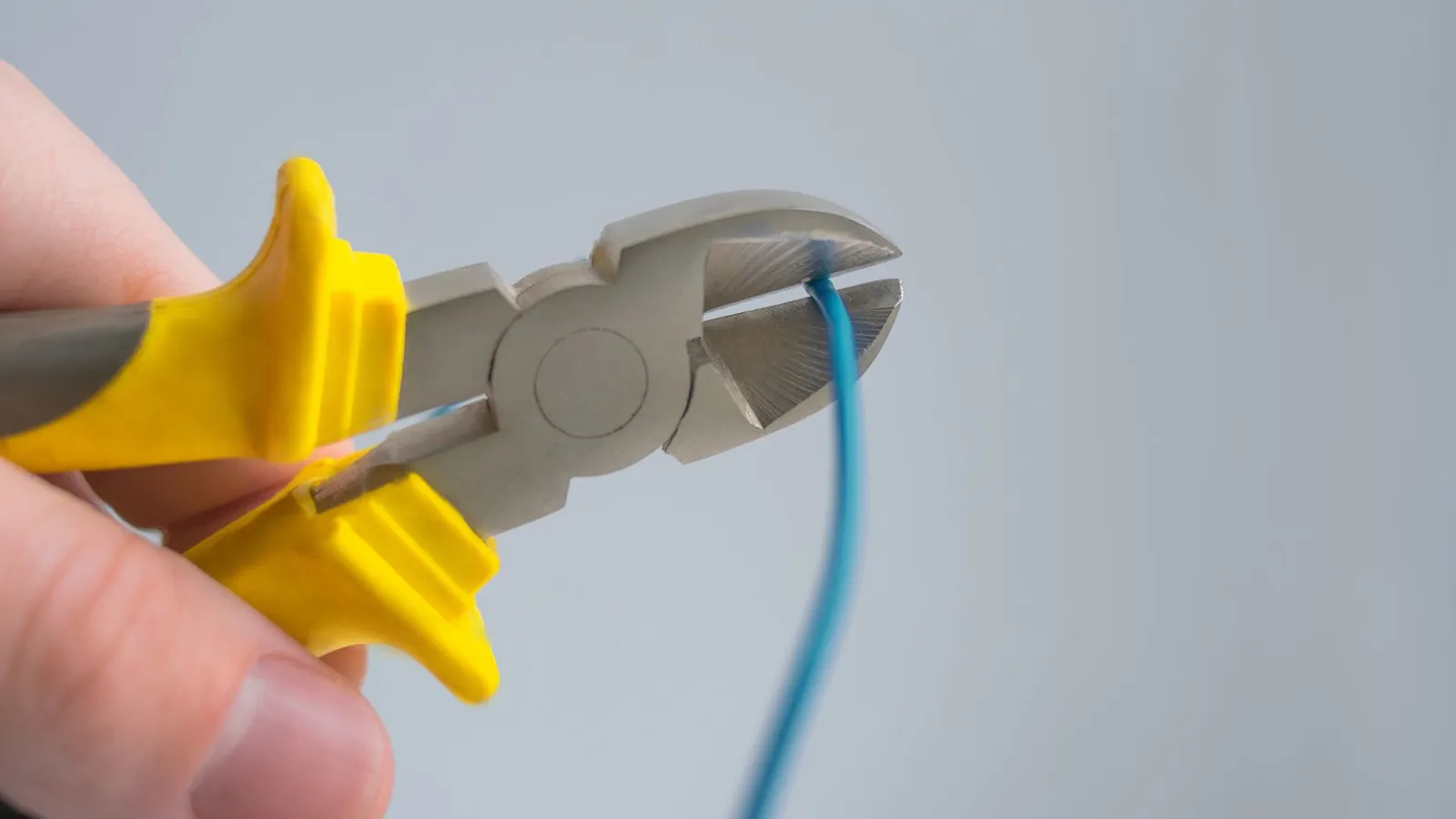 Pince coupante à poignées jaunes sectionnant un fil électrique bleu, en gros plan