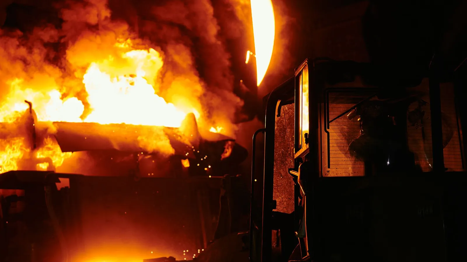 Coulée de métal en fusion dans une aciérie, flammes et fumées orangées autour de la poche