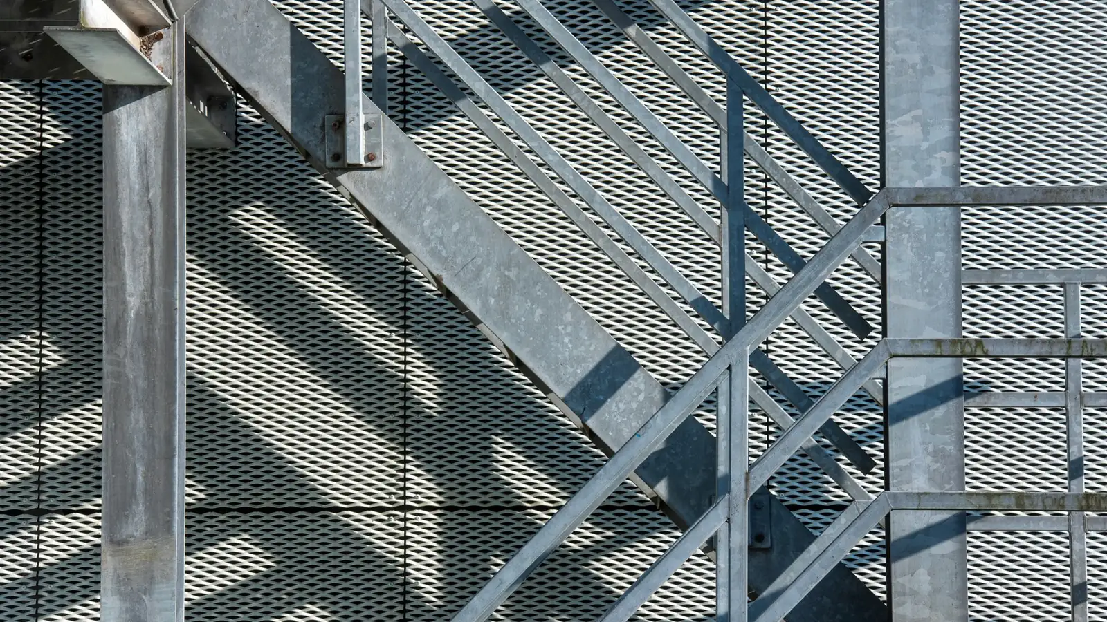 Escalier métallique galvanisé à limons en profilés et marches en caillebotis, devant un bardage en métal déployé