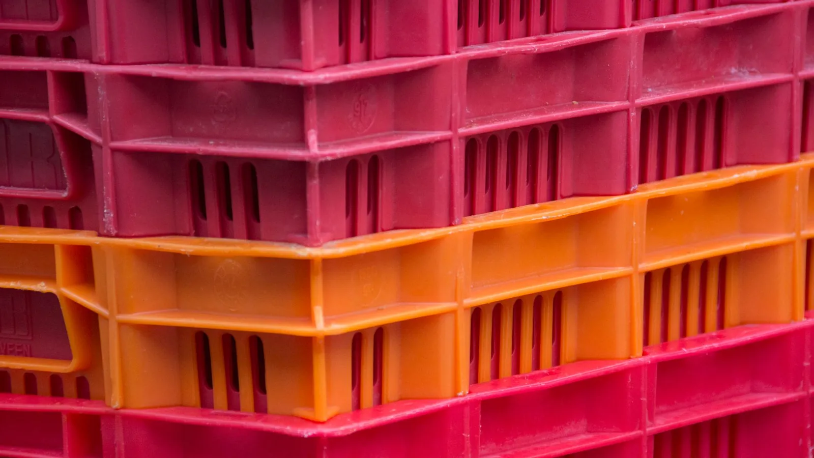 Caisses plastiques injectées empilées, roses et orange, aux parois ajourées et nervurées