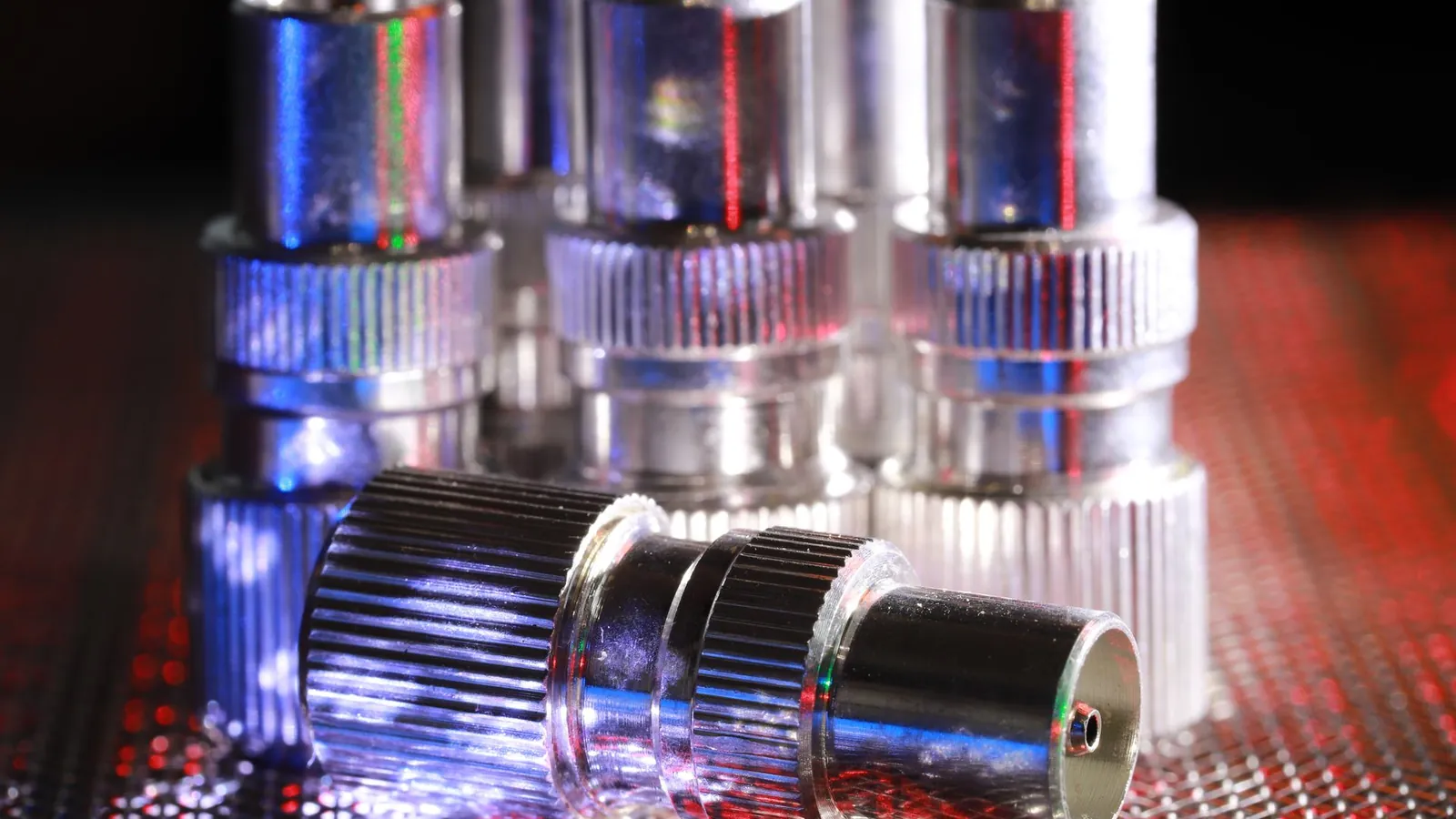 Connecteurs métalliques à revêtement brillant posés debout et couchés sur une grille, lumière bleutée