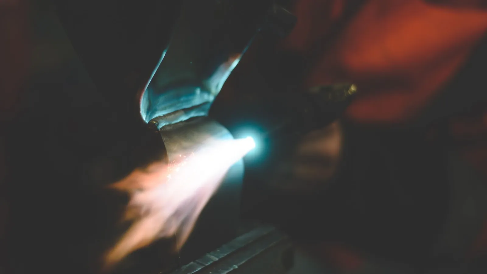 Flamme de chalumeau oxygaz projetée sur une pièce métallique dans la pénombre d'un atelier