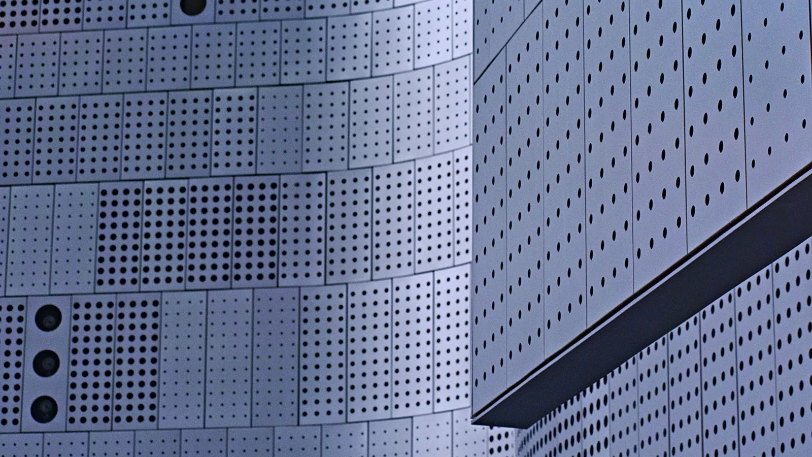 Cassettes de façade en tôle perforée aux bords pliés, assemblées en bandeaux courbes